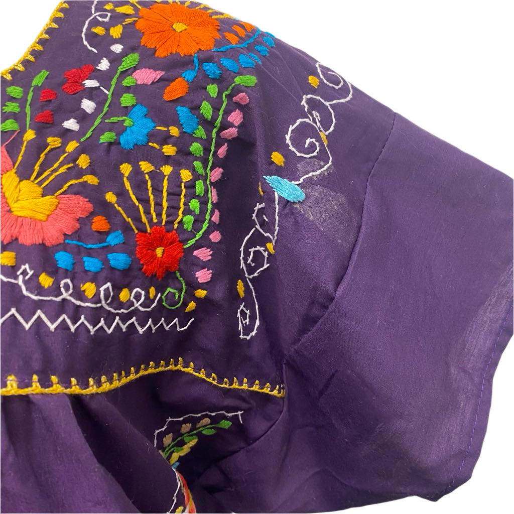 Purple fabric with colorful embroidered floral patterns on a plain background