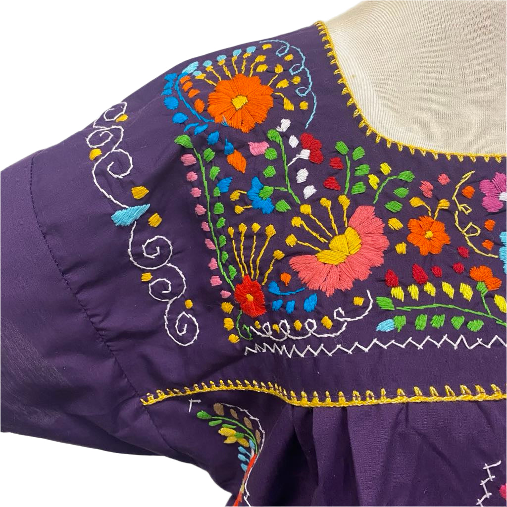 Close-up of a purple garment with colorful floral embroidery on a white background